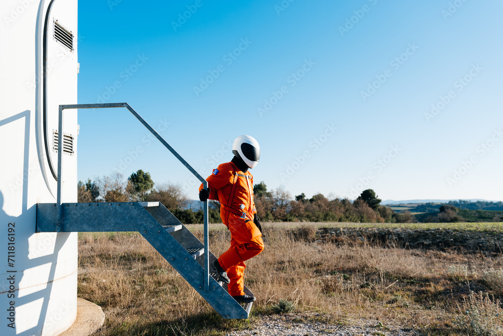 Man in aerospace helmet and uniform walking along metal stair of turbine in field