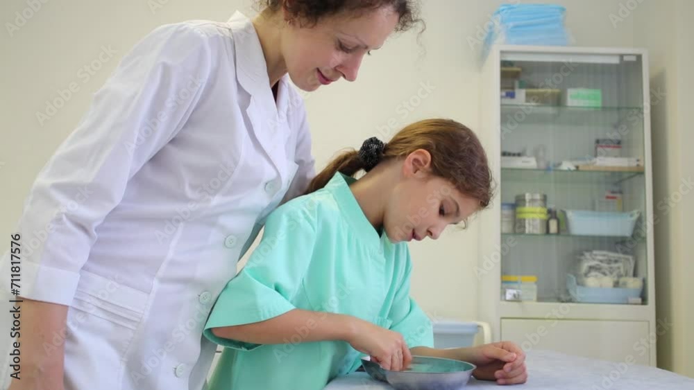 Girl and health worker look at content of metal bowl Girl and health worker look at content of metal bowl
