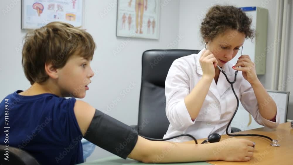Female doctor in white lab coat measures blood pressure of boy. Female doctor in white lab coat measures blood pressure of boy.