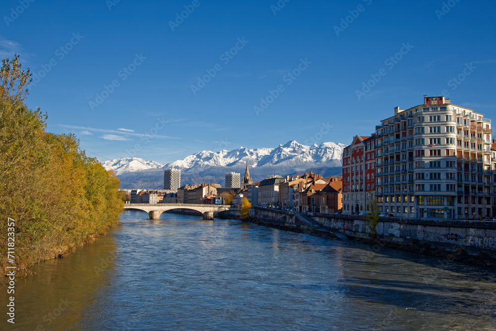 Fototapeta premium GRENOBLE, FRANCE, November 29, 2023 : Isere river and Grenoble city center with snowy mountains landscape in the background