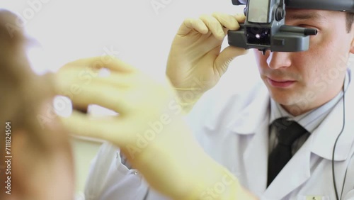 Ophthalmologist with indirect ophthalmoscope inspects girl eye. photo