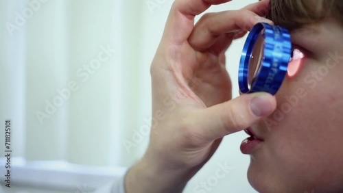 Hand of ophthalmologist with lens and boy face. Oculist examine eye photo