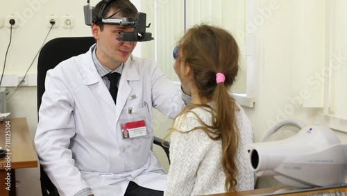 Ophthalmologist examines girl eye through ophthalmoscope. photo
