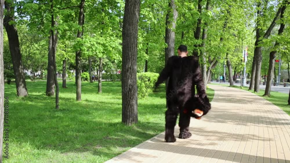Actor dressed as bear walks along pathway holding suit head 