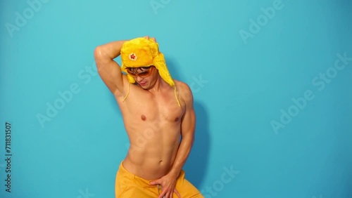 Half-naked guy in fur yellow cap and glasses dances in blue studio
