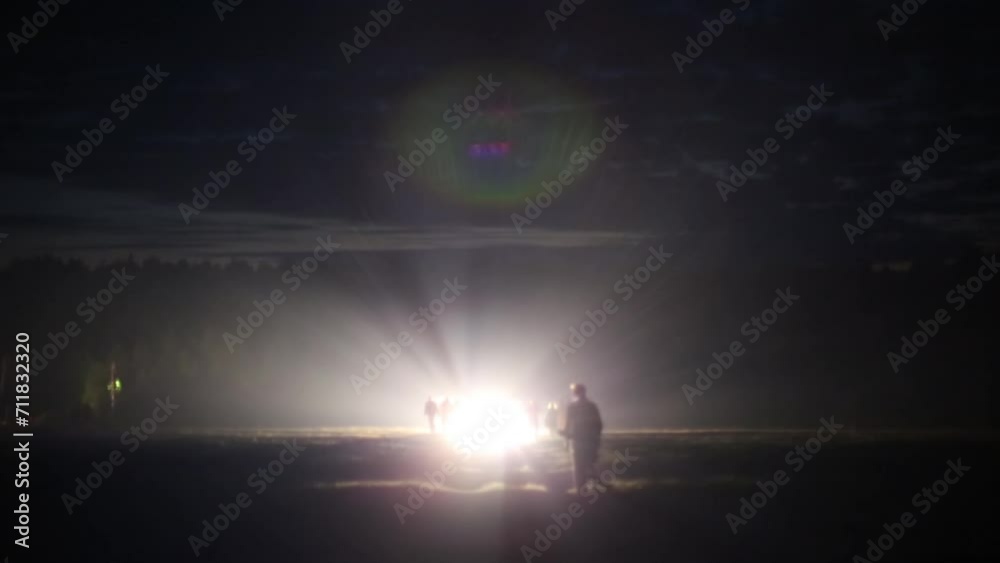 Silhouettes of people in field in rays of headlights of cars