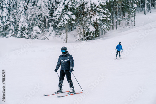 Skiers in equipment ski down the slope of a snowy mountain at the edge of the forest