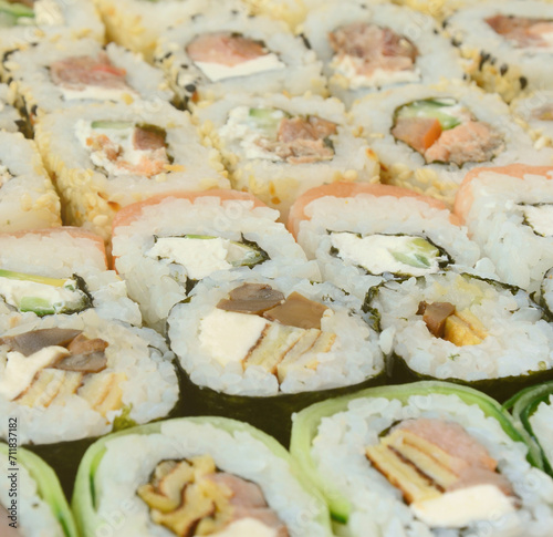 Close-up of a lot of sushi rolls with different fillings lie on a wooden surface. Macro shot of cooked classic Japanese food with a copy space.