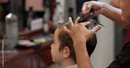 Hairdresser cuts hair, combs it. Attractive man getting his hair cut in a modern barbershop. Barber man cuts hair of cute little boy child. Stylish boy sitting in a hairdresser. 4K