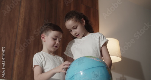 Children is studying while sitting at home in rays sunset in room. Kids in morning light sunset with Globe, Cute boy and little girl, technology for school boy, child looks at globe. 4K