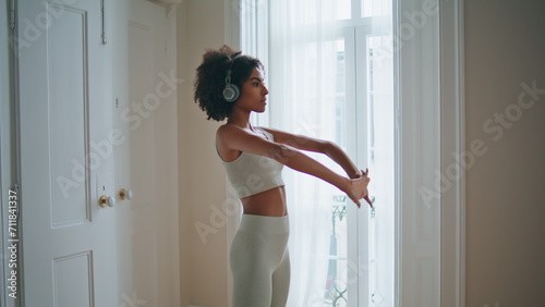 African lady stretching hands domestic place. Sportswear woman listening music