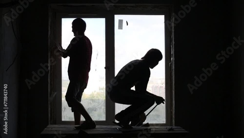 Silhouettes of two workers who dismantle old window frame. photo