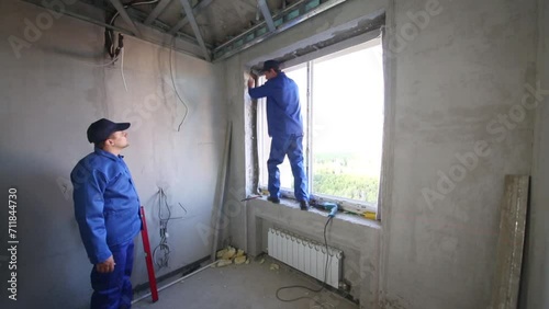 Two workers install window frame and check vertical accuracy photo