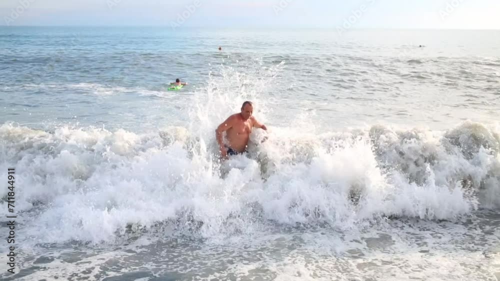 Elderly man stands near the shore in the sea, shows his hand in the sea and waits wave Elderly man stands near the shore in the sea, shows his hand in the sea and waits wave