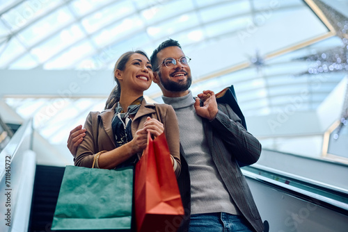 Happy couple moving down on escalator while shopping at mall. photo