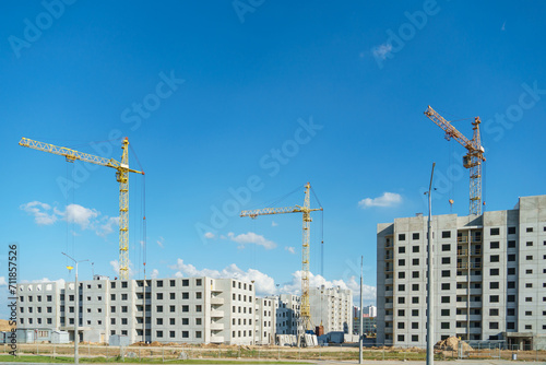 Silhouettes of working construction cranes against the background of an unfinished residential building. Multi-storey luxury apartment building on a construction site