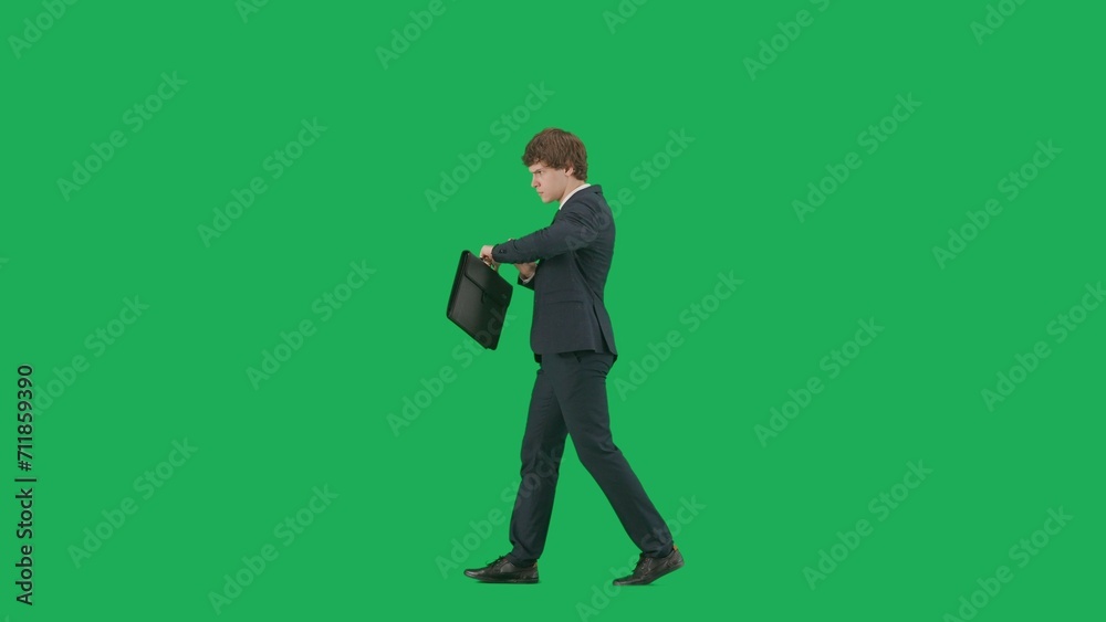 Modern businessman concept. Portrait of a male model in a suit against a green screen background with chroma key. Stylish businessman in a suit walks and looks at his watch, is late, is worried. Modern businessman concept. Portrait of a male model in a suit against a green screen background with chroma key. Stylish businessman in a suit walks and looks at his watch, is late, is worried.