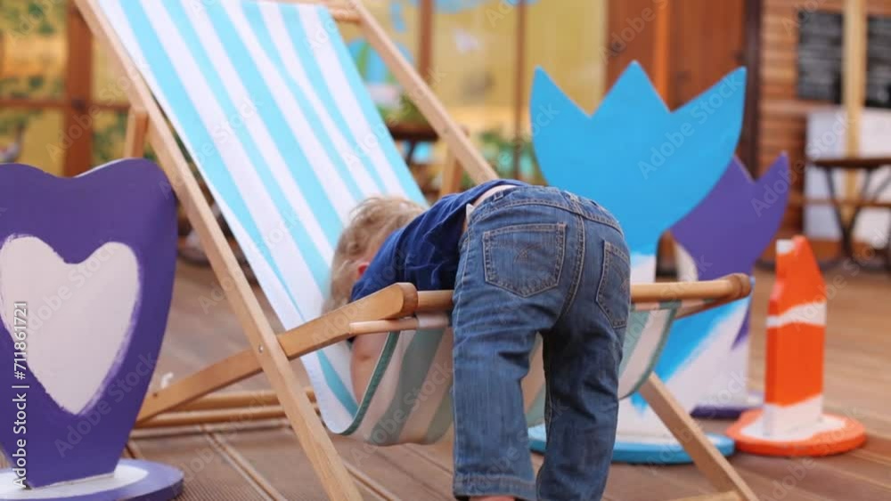 Little boy tries to get out of sun lounger in cafe with veranda