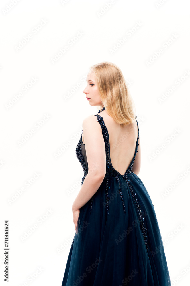 Young blonde woman in a dark blue ball gown with a fluffy skirt on a white background