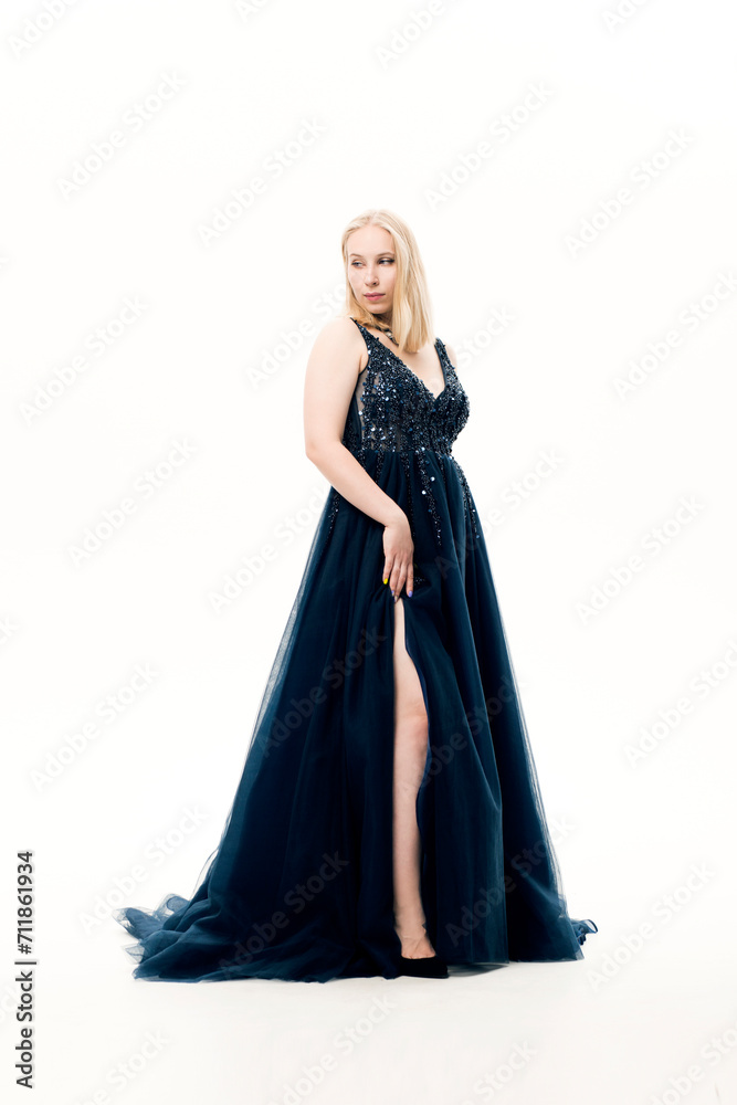 Young blonde woman in a dark blue ball gown with a fluffy skirt on a white background