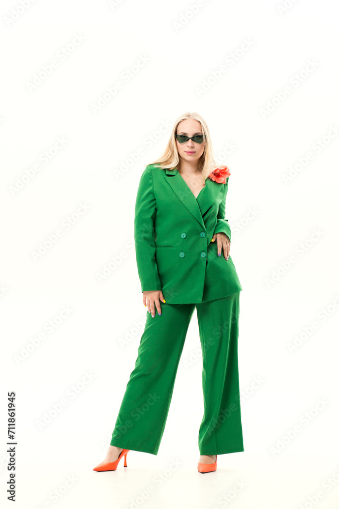 Young blonde woman in a green pantsuit and glasses on a white background