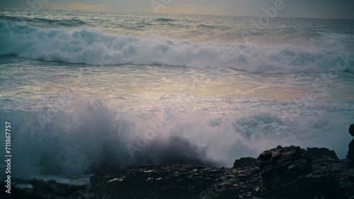 Foaming waves breaking coastline stones close up. Powerful ocean rolling shore
