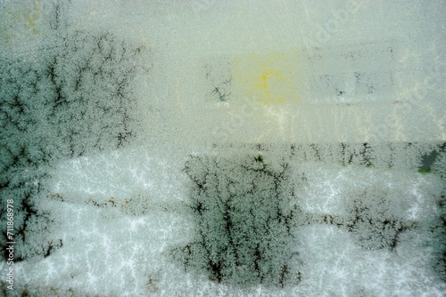 Abstraktes Motiv mit feuchter Glasscheibe und Eismuster vor Schneebedeckter Gartenlandschaft mit Wiese und Busch vor weißem Wohnhaus bei Frost und Schnee am Morgen im Winter photo