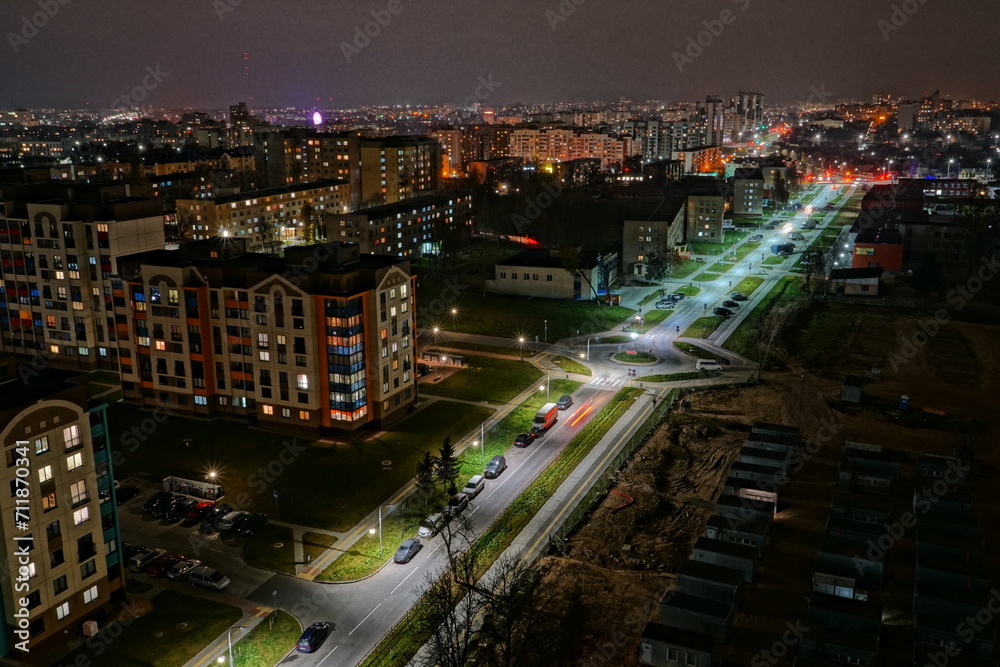 The lights of the night city. View of the busy city traffic and the light from the headlights of cars at night. The lights are on in the windows of residential buildings.