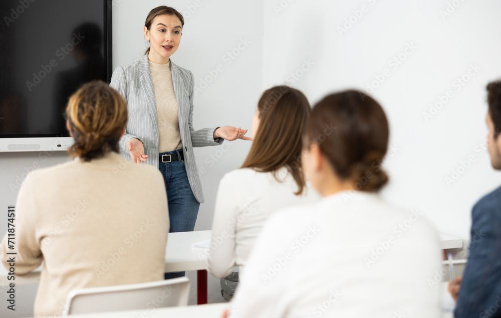 Young female tutor teaching students in college classroom
