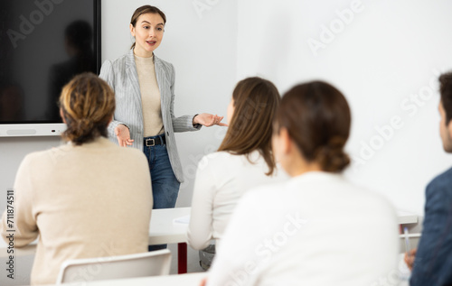 Young female tutor teaching students in college classroom