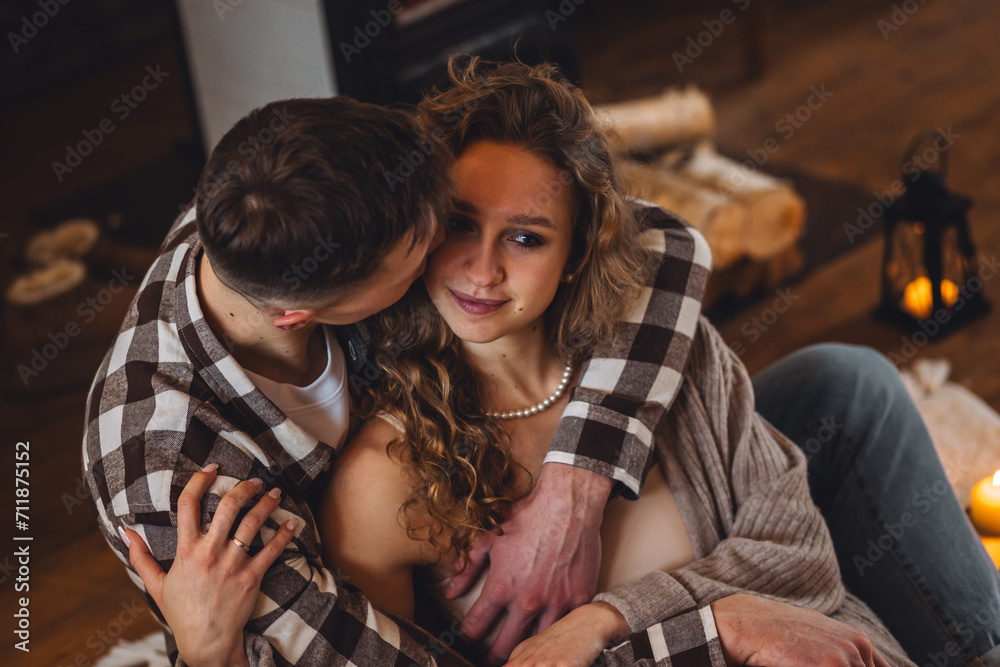 Beautiful young loving couple having breakfast, drinking hot chocolate with marshmallow in bed at home. Happy spouses enjoying lazy romantic winter morning in bedroom. Candles, garland, cozy fireplace
