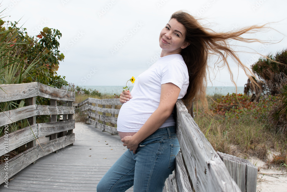 Happy pregnant Caucasian woman with a flower holding her baby bump. Third-trimester pregnancy