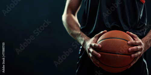 A focused athlete in a dark jersey holds a basketball against a dark background, emphasizing the readiness and determination for the game.