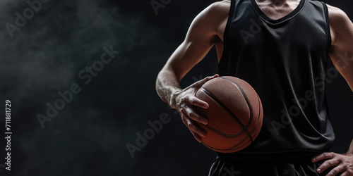 A focused athlete in a dark jersey holds a basketball against a dark background, emphasizing the readiness and determination for the game.