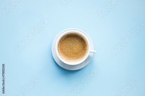 On a blue background there is a white cup with hot, aromatic, delicious cappuccino coffee. Flat lay, top view, close-up. Concept coffee break, hot drinks. Space for copying text.

