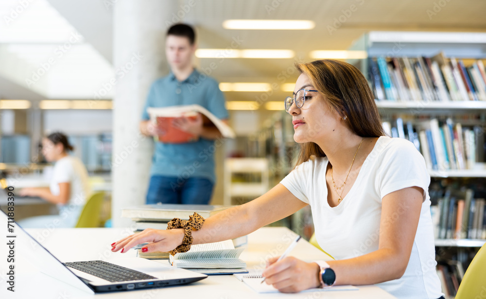 Obraz premium Mexican school student girl doing research on project in the college library..