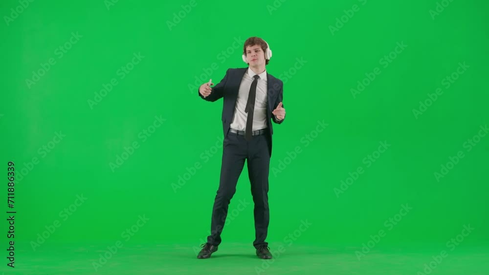 Portrait of male model in suit on chroma key green screen. Handsome young businessman in suit listens music in headphones on smartphone, dancing. Portrait of male model in suit on chroma key green screen. Handsome young businessman in suit listens music in headphones on smartphone, dancing.
