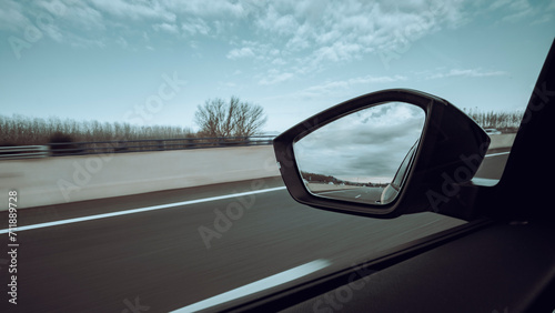 Left side window view scene of a road car on a highway on a beautiful forest landscape with sharp backward mirror