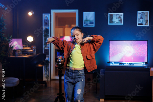 Little girl doing content creation for children, utilizing smartphone on tripod to produce dance videos for online streaming platforms. Cute kid creating trending choreography with cellphone photo