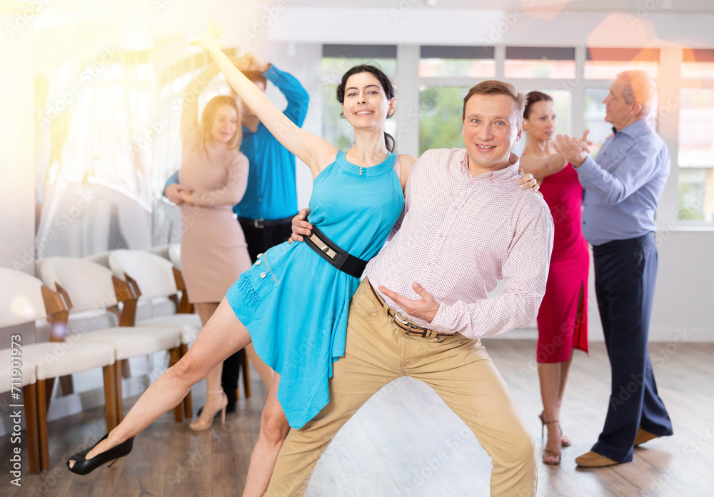 Positive men and woman dancing slow ballroom dance during group class in choreography studio