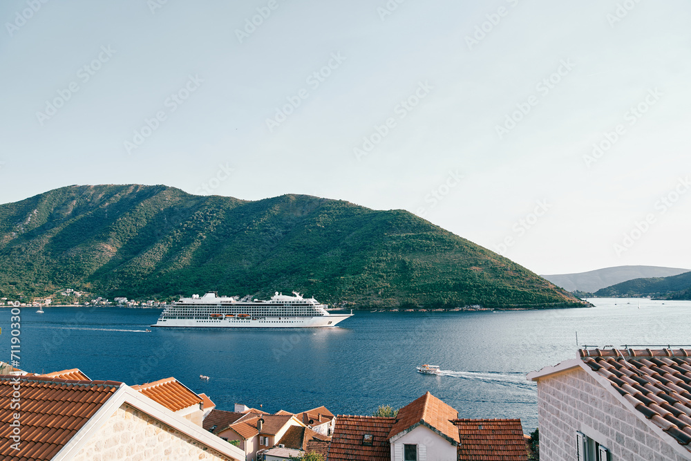 View over the red roofs of houses to a white cruise ship sailing on the sea along the mountains
