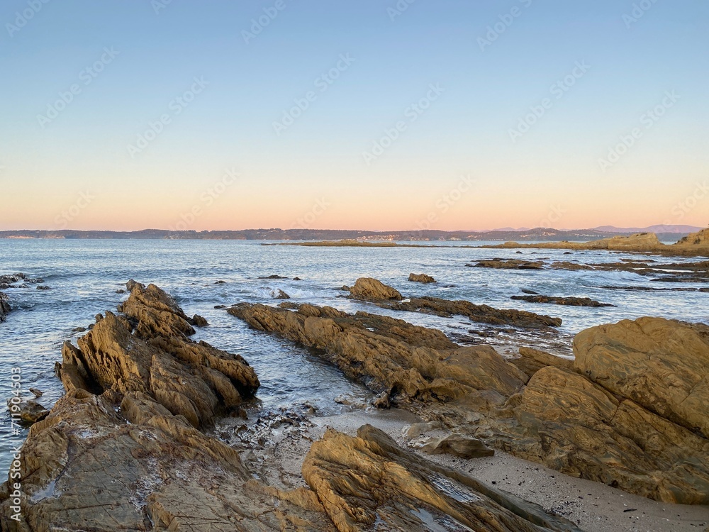 Sunset at the beach. Dawn on the beach. Waves curling on the rocky shore. Ocean view at low tide.