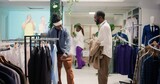 Client shopping in luxurious clothing store with elegant assortment of blazers, helped by friendly employee. Woman helping man try on clothes in premium fashion boutique with stylish attire garments