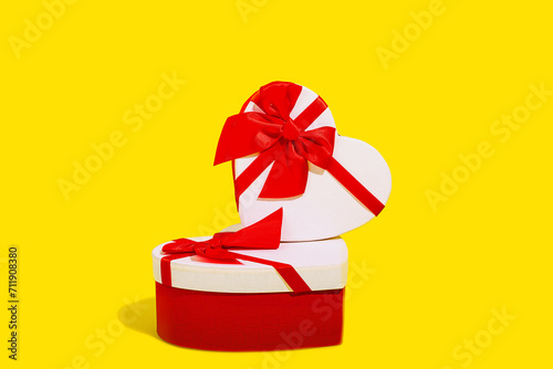 A stacked arrangement of two heart shaped gift boxes with vibrant red ribbons on a yellow background photo