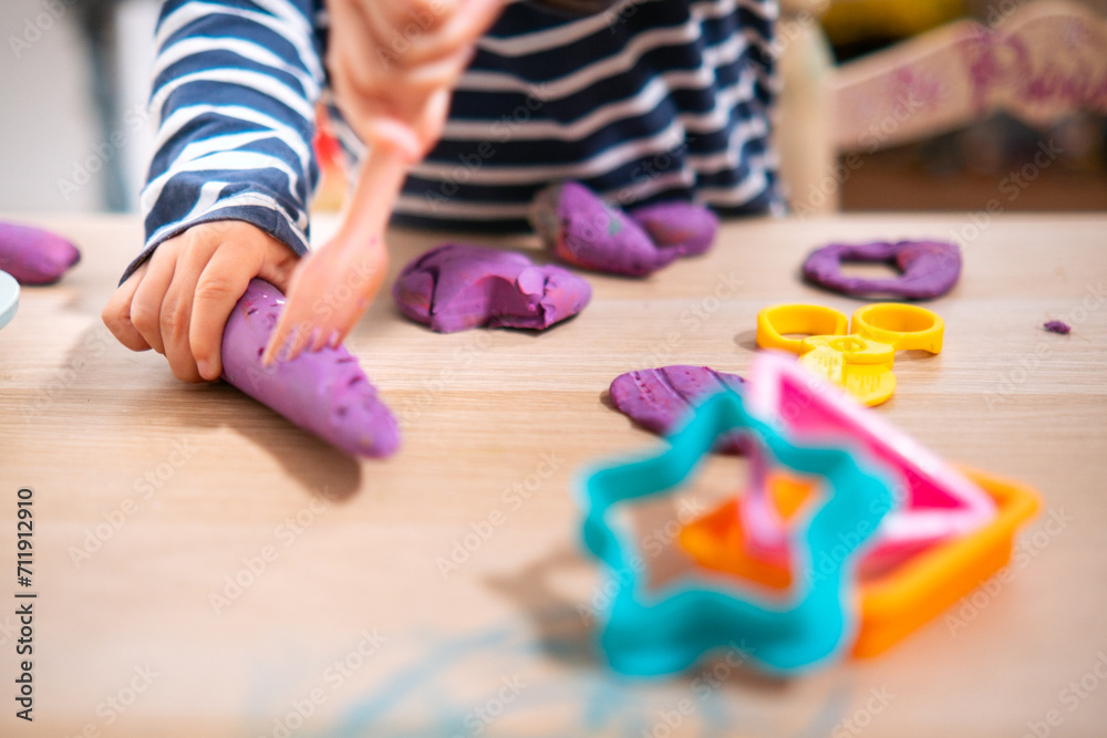 Manos de niña de  2 años jugando con plastilina casera y moldes. Jugar con la plastifica en casa, juguetes educativos para niños Montessori. Juegos creativos para niños pequeños. 