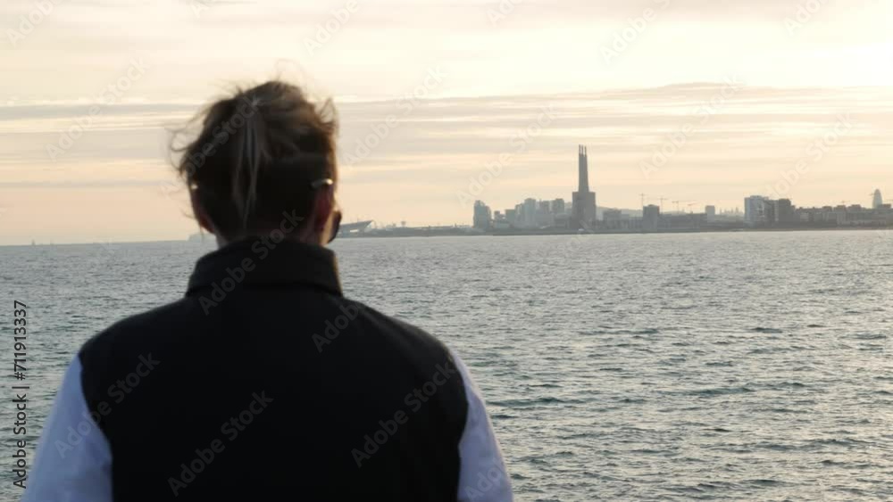Close-up of a girl from the back, looking at the sunset by the sea and the city