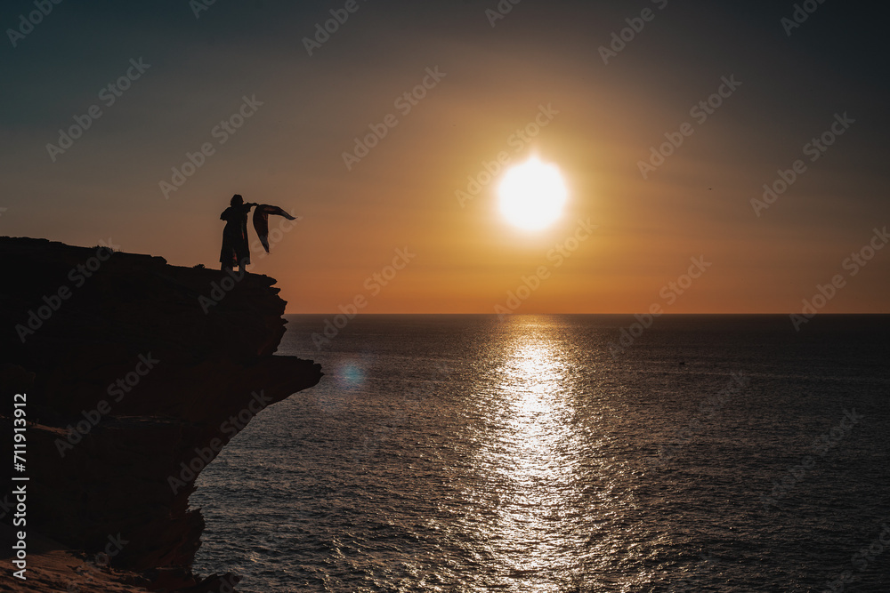 Silhouette of a person standing on a rock during a sunset.