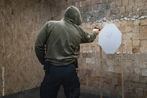 Tactical shooting, a man in a hood shoots with one hand at a paper target from close range in a shooting range. photo