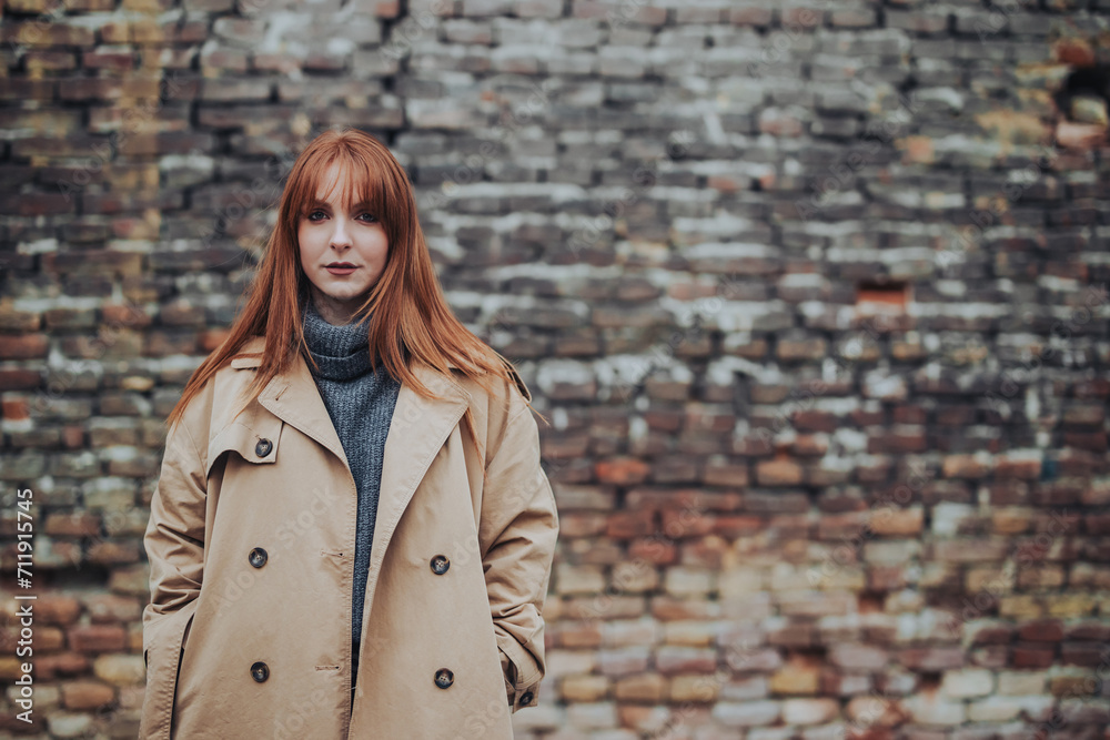 Fashion photo of a young redhead woman posing near rustic wall.