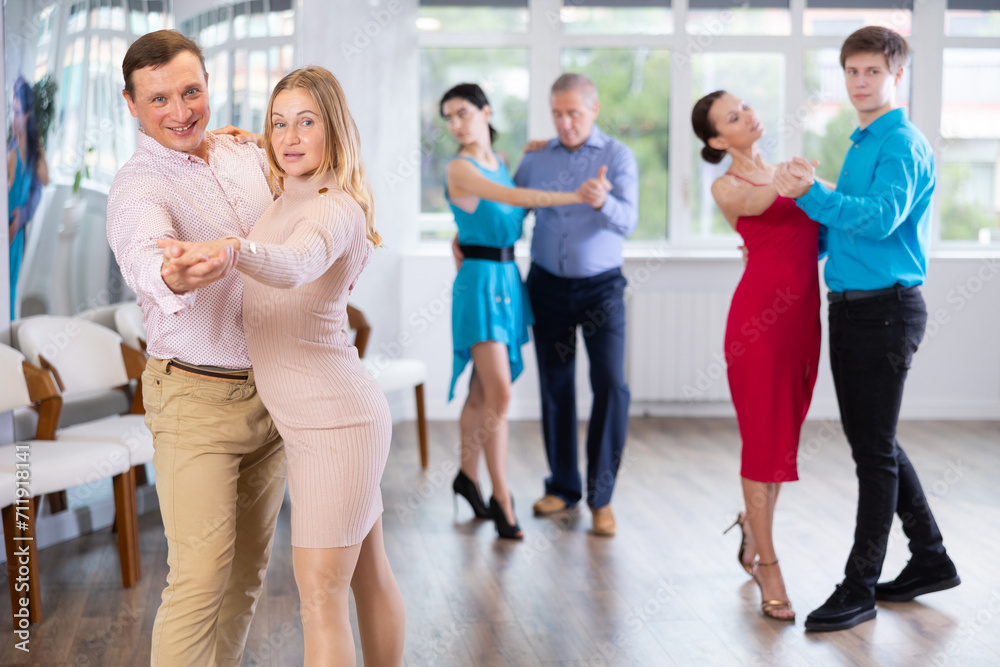 Obraz premium Positive adult couple enjoying slow foxtrot in dance studio. Amateur social dancing concept..